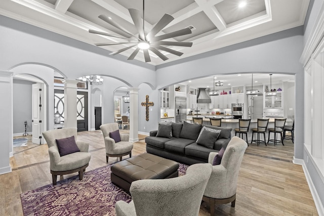 living room with arched walkways, coffered ceiling, light wood-style floors, a towering ceiling, and ornate columns