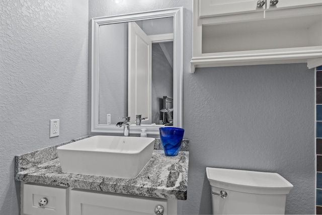 half bath featuring a textured wall, vanity, and toilet