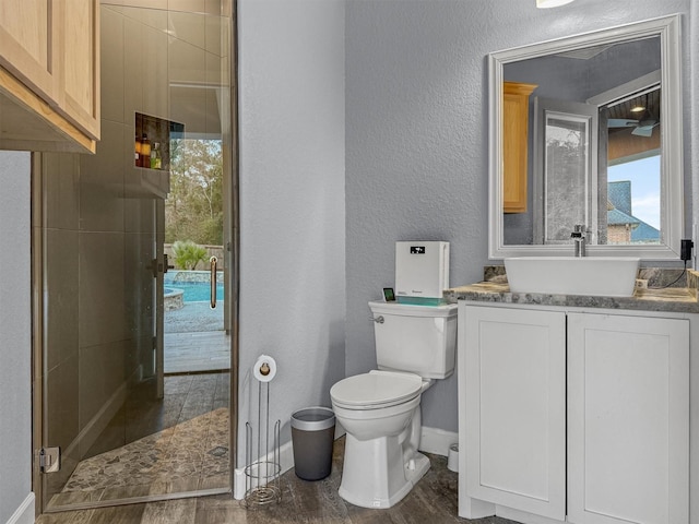 bathroom with a textured wall, toilet, a stall shower, vanity, and baseboards