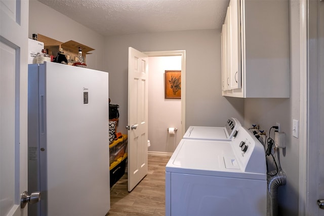 washroom with a textured ceiling, light wood-style flooring, independent washer and dryer, and cabinet space