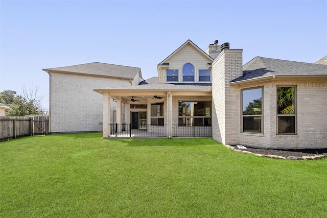 rear view of house featuring ceiling fan, a fenced backyard, brick siding, a lawn, and a chimney