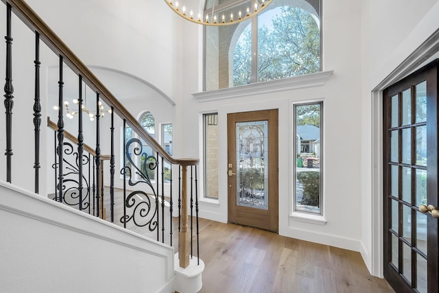 entryway featuring baseboards, an inviting chandelier, stairs, a high ceiling, and light wood-type flooring