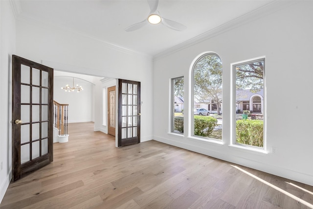 empty room featuring light wood-style flooring, ornamental molding, baseboards, and ceiling fan with notable chandelier