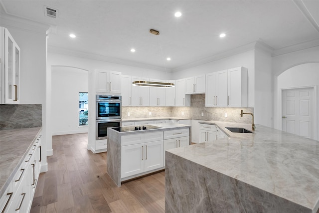 kitchen featuring arched walkways, stainless steel double oven, light wood-style flooring, a sink, and white cabinets