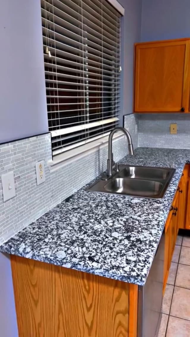 kitchen with backsplash, brown cabinetry, a sink, and light tile patterned flooring