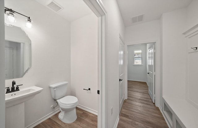 half bath with toilet, visible vents, and wood finished floors