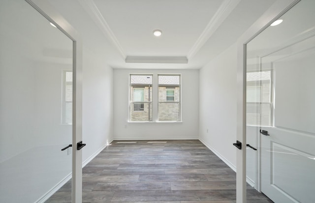 spare room featuring ornamental molding, a tray ceiling, wood finished floors, and baseboards