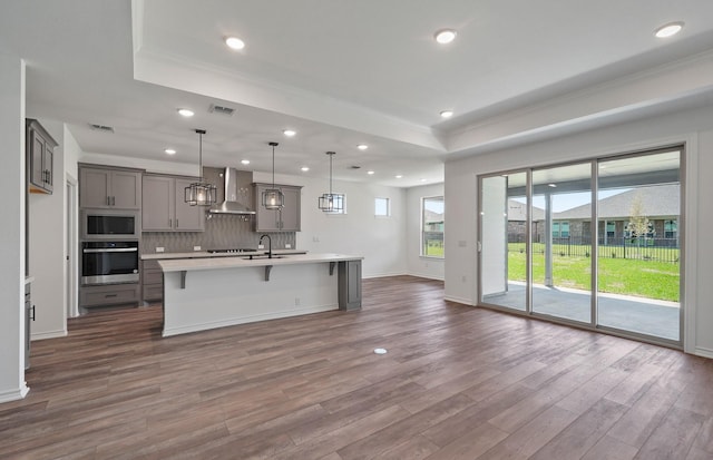 kitchen featuring a raised ceiling, wall chimney exhaust hood, appliances with stainless steel finishes, and gray cabinets