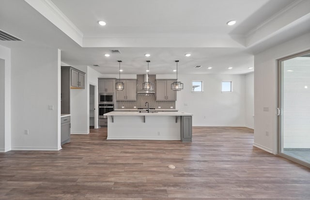 kitchen featuring wall chimney exhaust hood, a sink, gray cabinetry, and wood finished floors