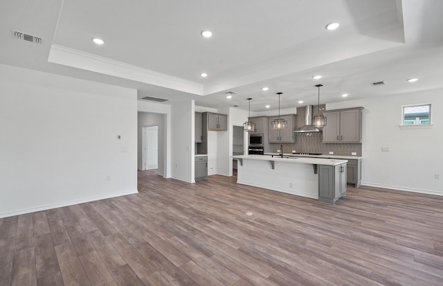 kitchen featuring visible vents, a raised ceiling, wood finished floors, gray cabinets, and wall chimney range hood