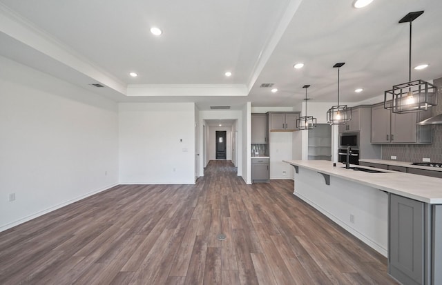 kitchen with dark wood-type flooring, gray cabinets, a raised ceiling, and a sink