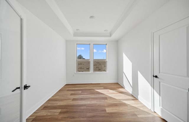 unfurnished room with light wood-type flooring, baseboards, a tray ceiling, and crown molding