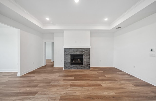 unfurnished living room with light wood-type flooring, a fireplace, a tray ceiling, and ornamental molding