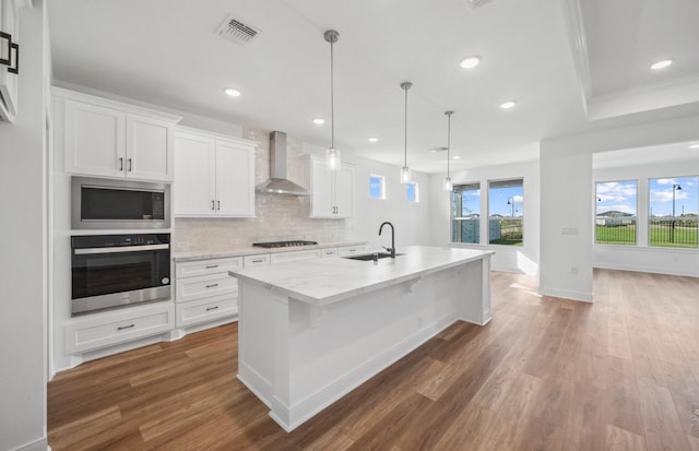 kitchen featuring stainless steel appliances, a sink, wall chimney exhaust hood, and wood finished floors