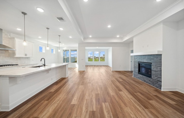 unfurnished living room featuring visible vents, baseboards, a brick fireplace, a tray ceiling, and light wood finished floors