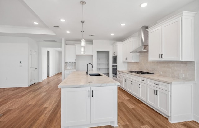 kitchen featuring light wood finished floors, wall chimney range hood, gas cooktop, a sink, and recessed lighting