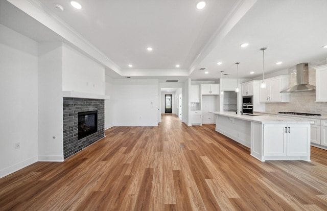 kitchen featuring a tray ceiling, gas stovetop, light countertops, open floor plan, and wall chimney exhaust hood