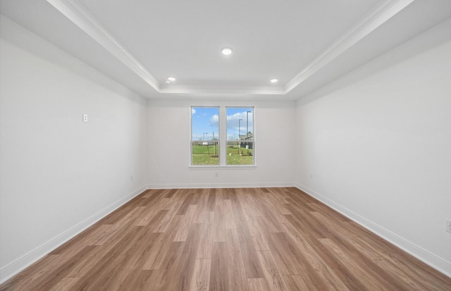 empty room featuring light wood-type flooring, a tray ceiling, crown molding, and baseboards