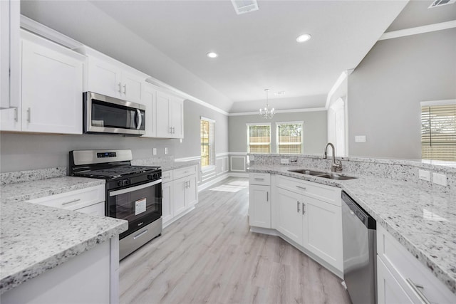 kitchen with light stone counters, a sink, white cabinets, appliances with stainless steel finishes, and crown molding