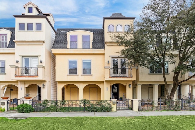 view of front of property with a shingled roof, a fenced front yard, a balcony, and stucco siding