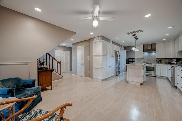 kitchen with stainless steel appliances, a kitchen island, white cabinets, hanging light fixtures, and wall chimney exhaust hood