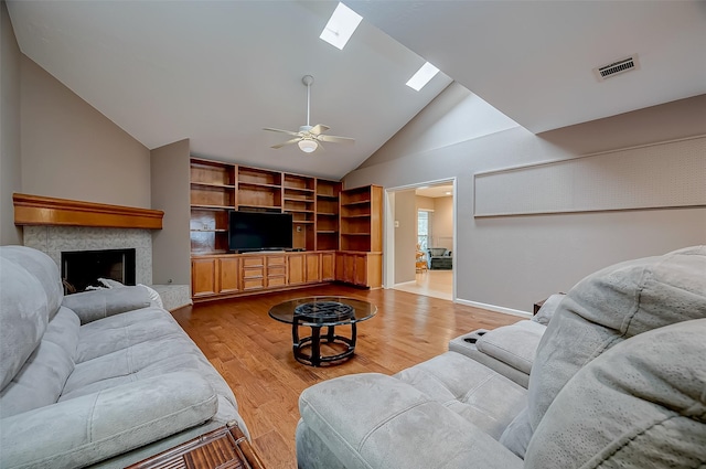 living area with a skylight, a fireplace, visible vents, light wood-style flooring, and a ceiling fan