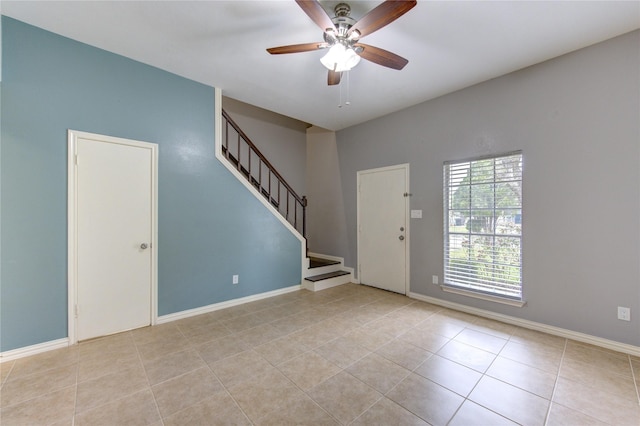 empty room featuring light tile patterned floors, baseboards, stairway, and a ceiling fan