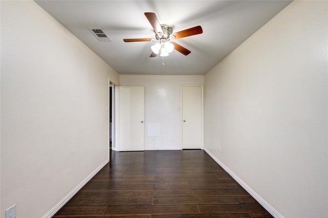 empty room with dark wood-style floors, ceiling fan, visible vents, and baseboards