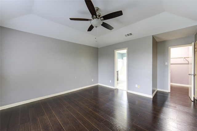 empty room with a raised ceiling, dark wood finished floors, visible vents, and baseboards