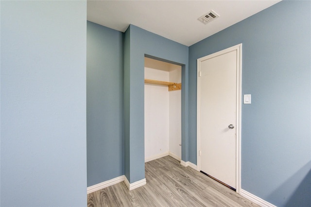 hall featuring light wood-style flooring, visible vents, and baseboards