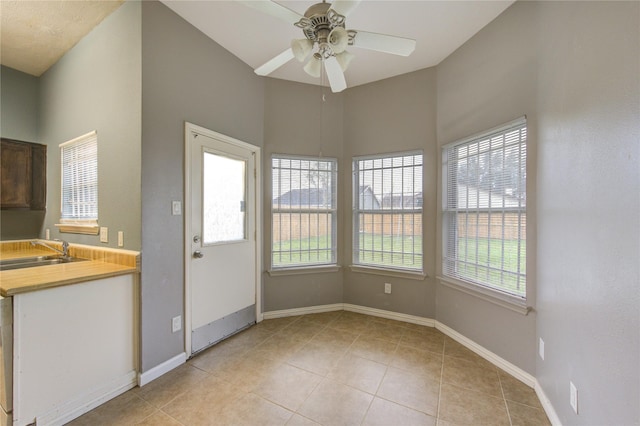 unfurnished dining area featuring light tile patterned flooring, a sink, a ceiling fan, and baseboards