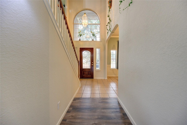 doorway featuring arched walkways, baseboards, light wood-style flooring, and a high ceiling