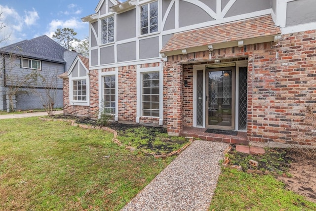 entrance to property with a yard, brick siding, and stucco siding