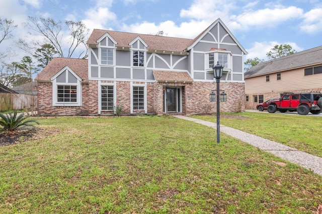 tudor-style house featuring brick siding, stucco siding, a shingled roof, fence, and a front lawn