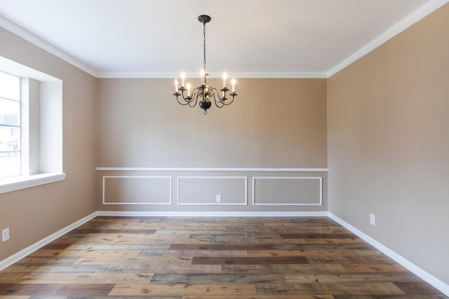 empty room with a chandelier, a decorative wall, wood finished floors, baseboards, and ornamental molding