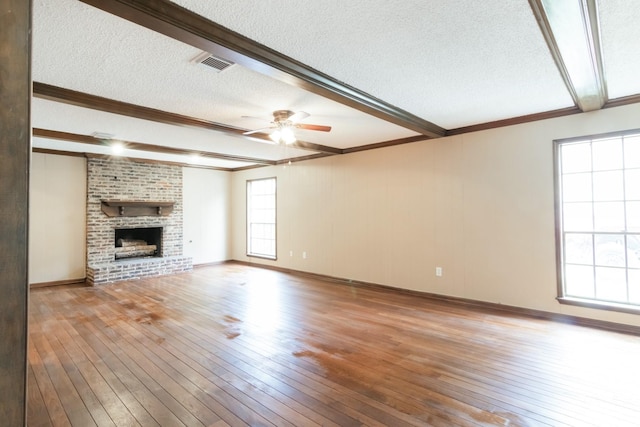 unfurnished living room with a textured ceiling, visible vents, light wood-type flooring, a brick fireplace, and beam ceiling