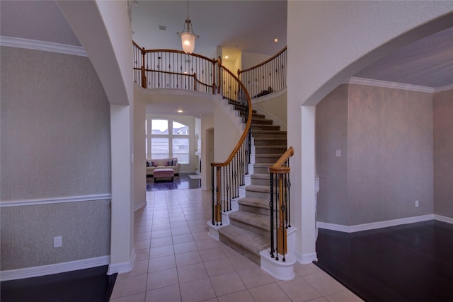 tiled entrance foyer featuring arched walkways, stairway, crown molding, and baseboards