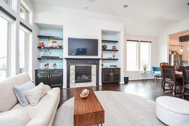 living area with built in features, visible vents, a glass covered fireplace, dark wood-style flooring, and vaulted ceiling