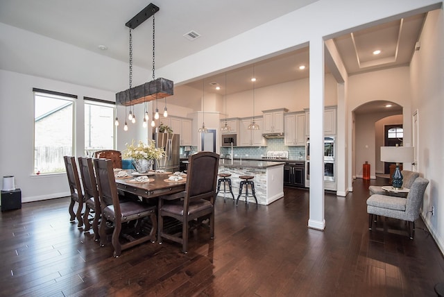 dining area with baseboards, visible vents, arched walkways, dark wood-style floors, and a high ceiling