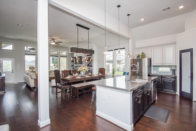 kitchen with light stone counters, visible vents, a kitchen island with sink, a sink, and stainless steel fridge with ice dispenser