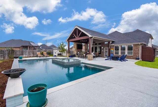 view of pool with a patio area, a fireplace, fence, and a pool with connected hot tub