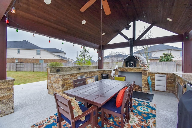 view of patio with an outdoor kitchen, a ceiling fan, fence, a gazebo, and outdoor dining space