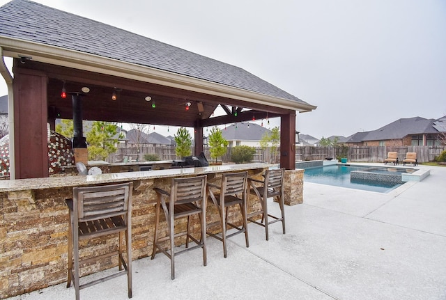 view of patio with a fenced backyard, a pool with connected hot tub, a gazebo, an outdoor bar, and a residential view