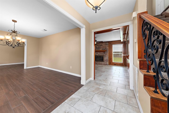 entryway featuring light wood-style flooring, a fireplace, baseboards, and ceiling fan with notable chandelier