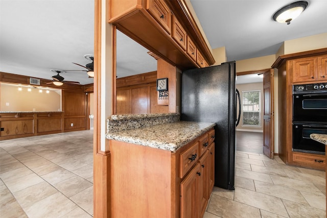 kitchen featuring light stone counters, visible vents, a ceiling fan, black appliances, and brown cabinetry