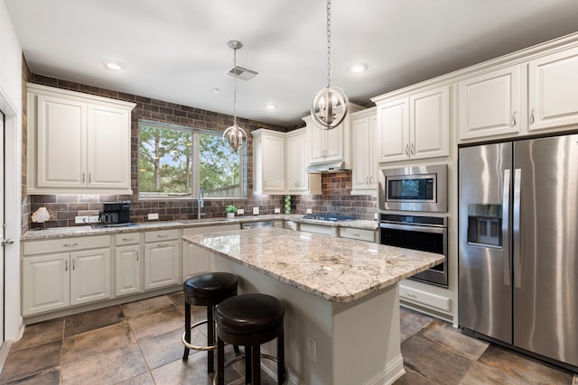 kitchen with a center island, decorative light fixtures, appliances with stainless steel finishes, white cabinets, and under cabinet range hood