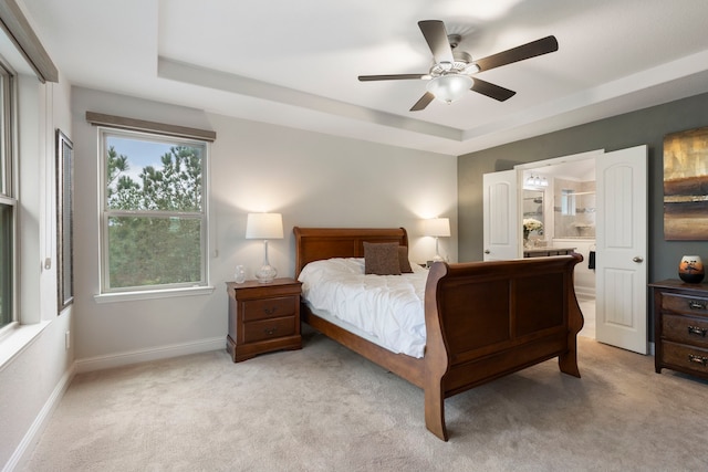 bedroom featuring a tray ceiling, light carpet, ceiling fan, and baseboards