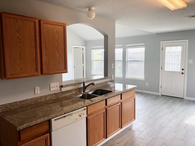 kitchen featuring stone countertops, brown cabinets, white dishwasher, light wood-type flooring, and a sink