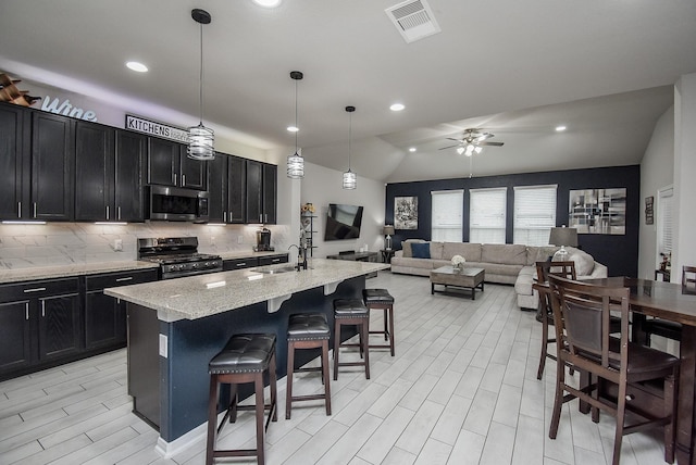 kitchen featuring a breakfast bar, pendant lighting, a center island with sink, stainless steel appliances, and open floor plan