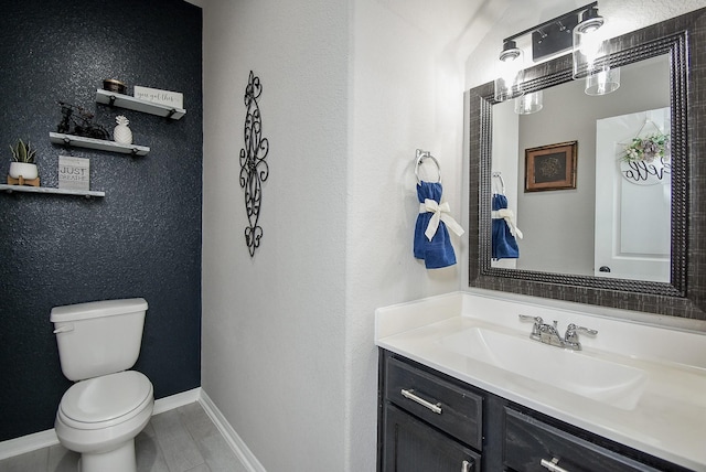 half bathroom with baseboards, vanity, and toilet